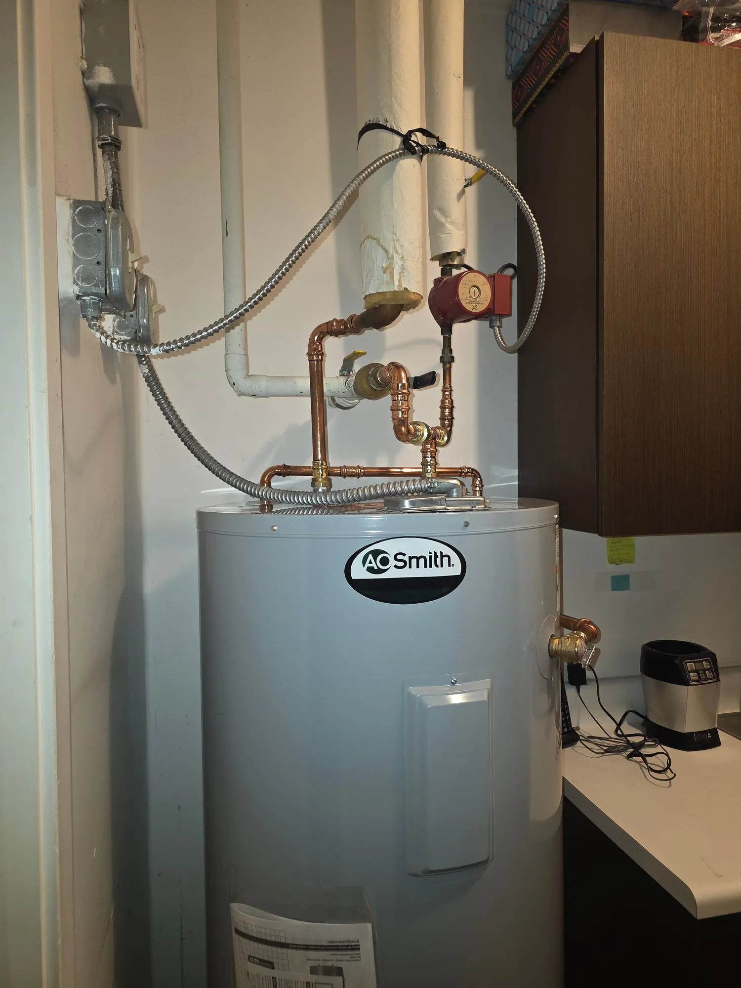 A. O. Smith electric water heater with copper piping and a recirculation pump in a closet