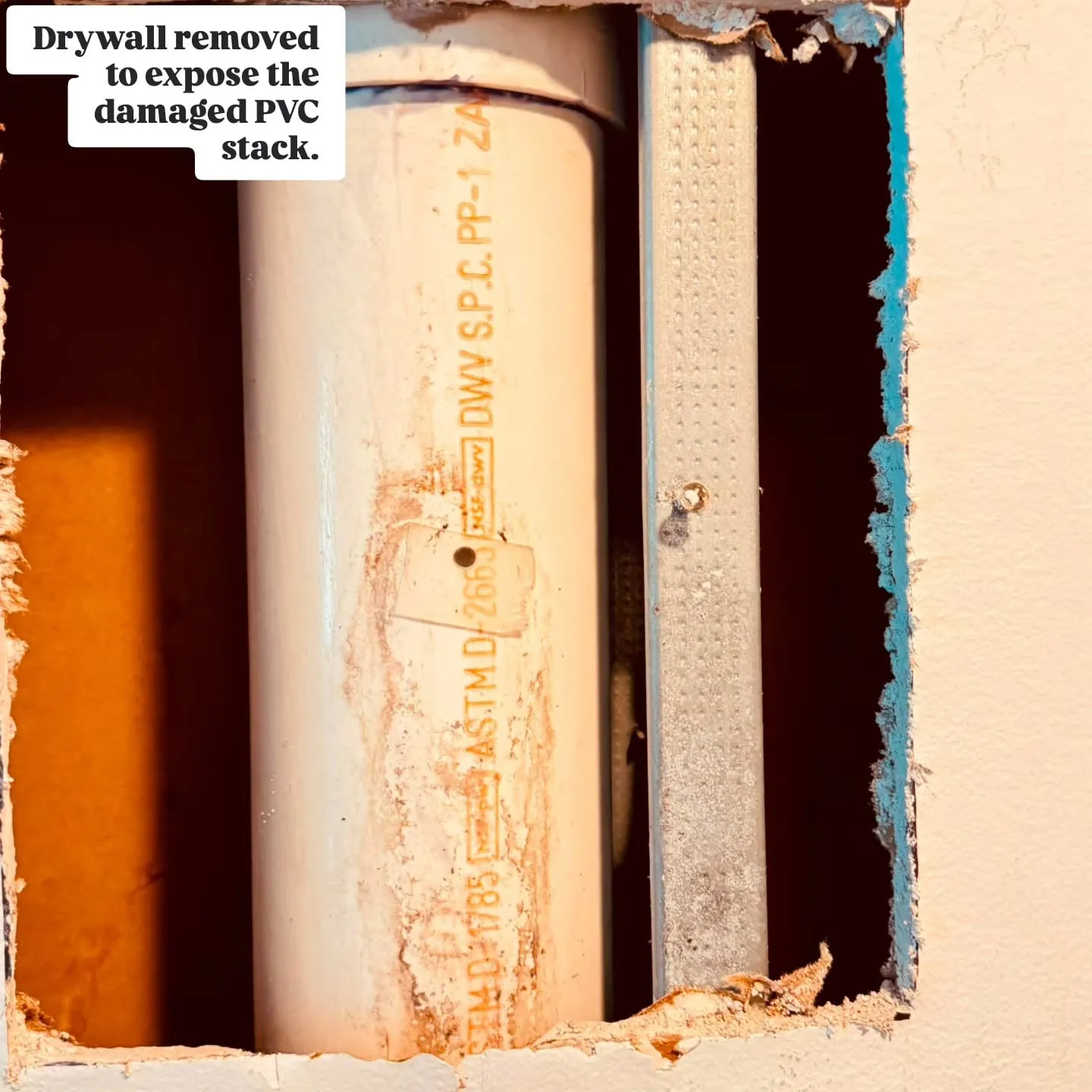Drywall cut away to expose a damaged white PVC drain stack