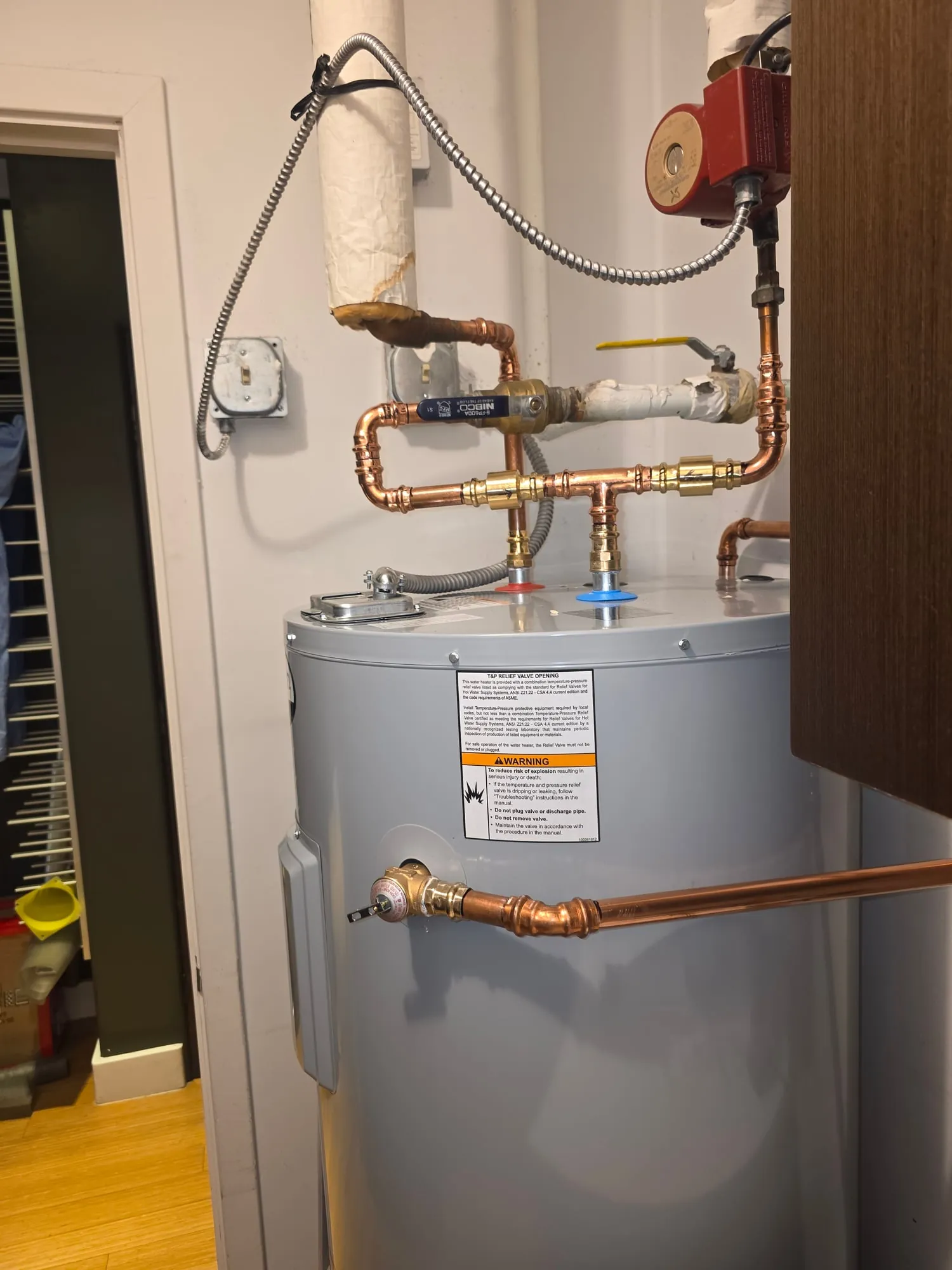 Copper piping with ball valves and a recirculation pump above an electric water heater