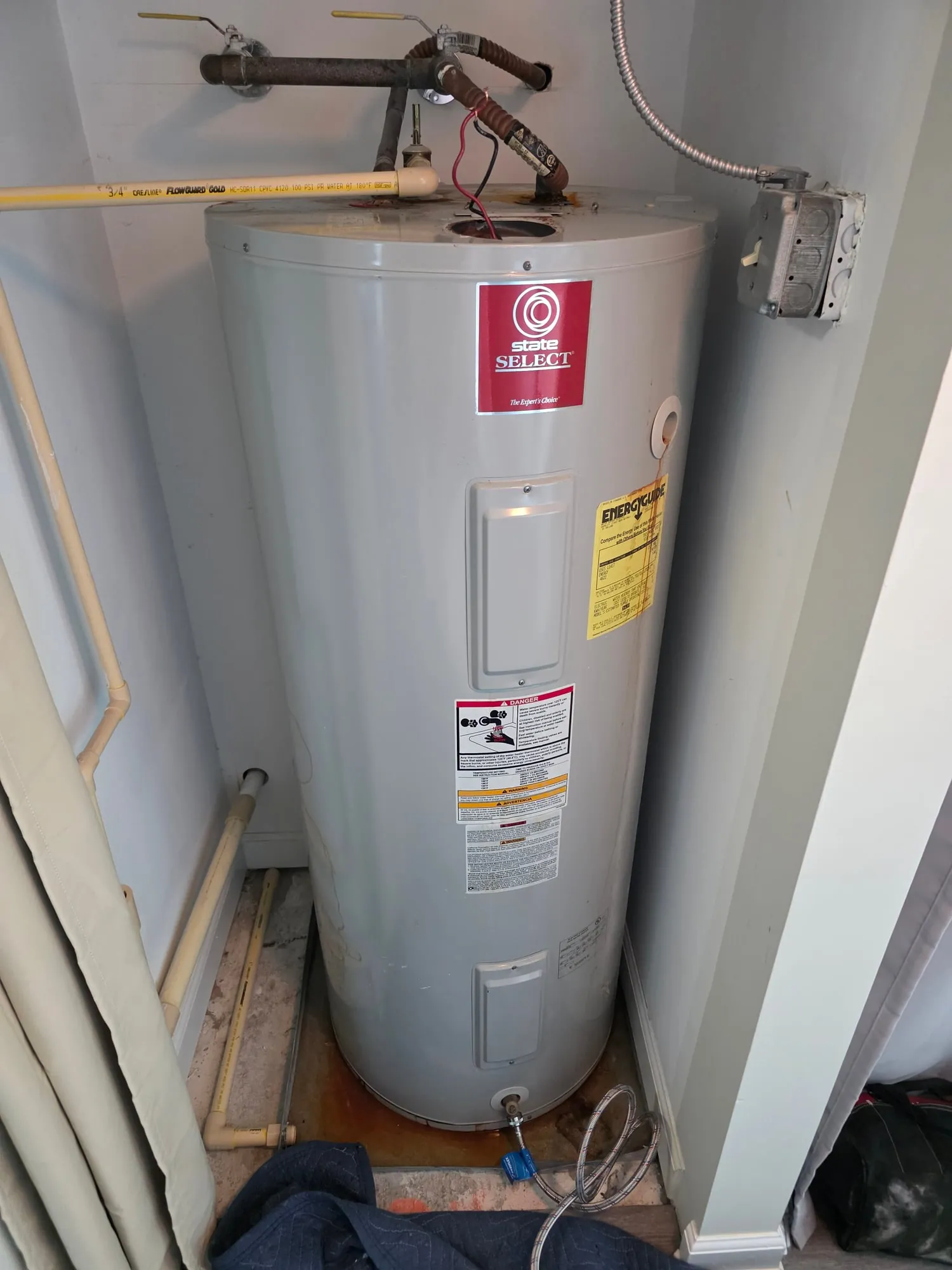 Electric water heater in a narrow hallway closet beside a curtain