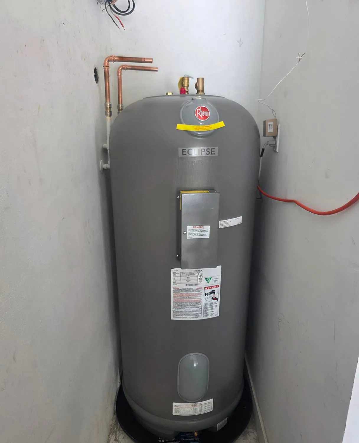 Tall Rheem electric water heater installed in a corner closet on a drain pan