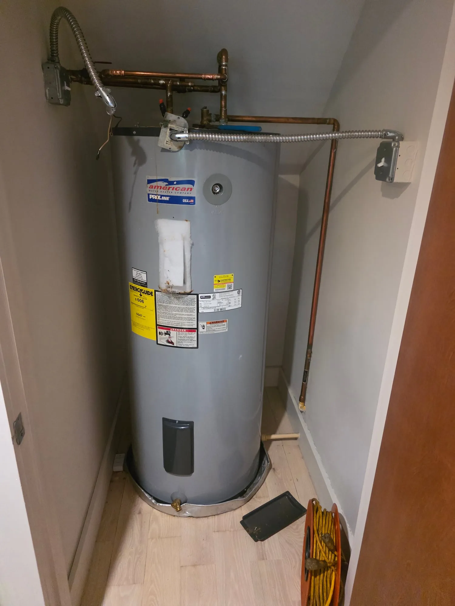 Tall electric water heater in a narrow closet with copper supply lines overhead
