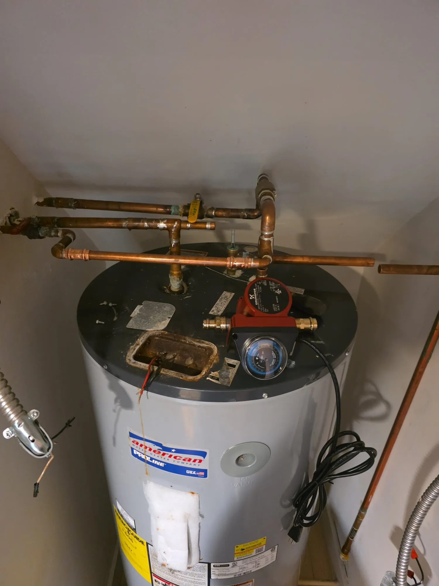 Electric water heater with a recirculation pump on top, in a closet with a sloped ceiling