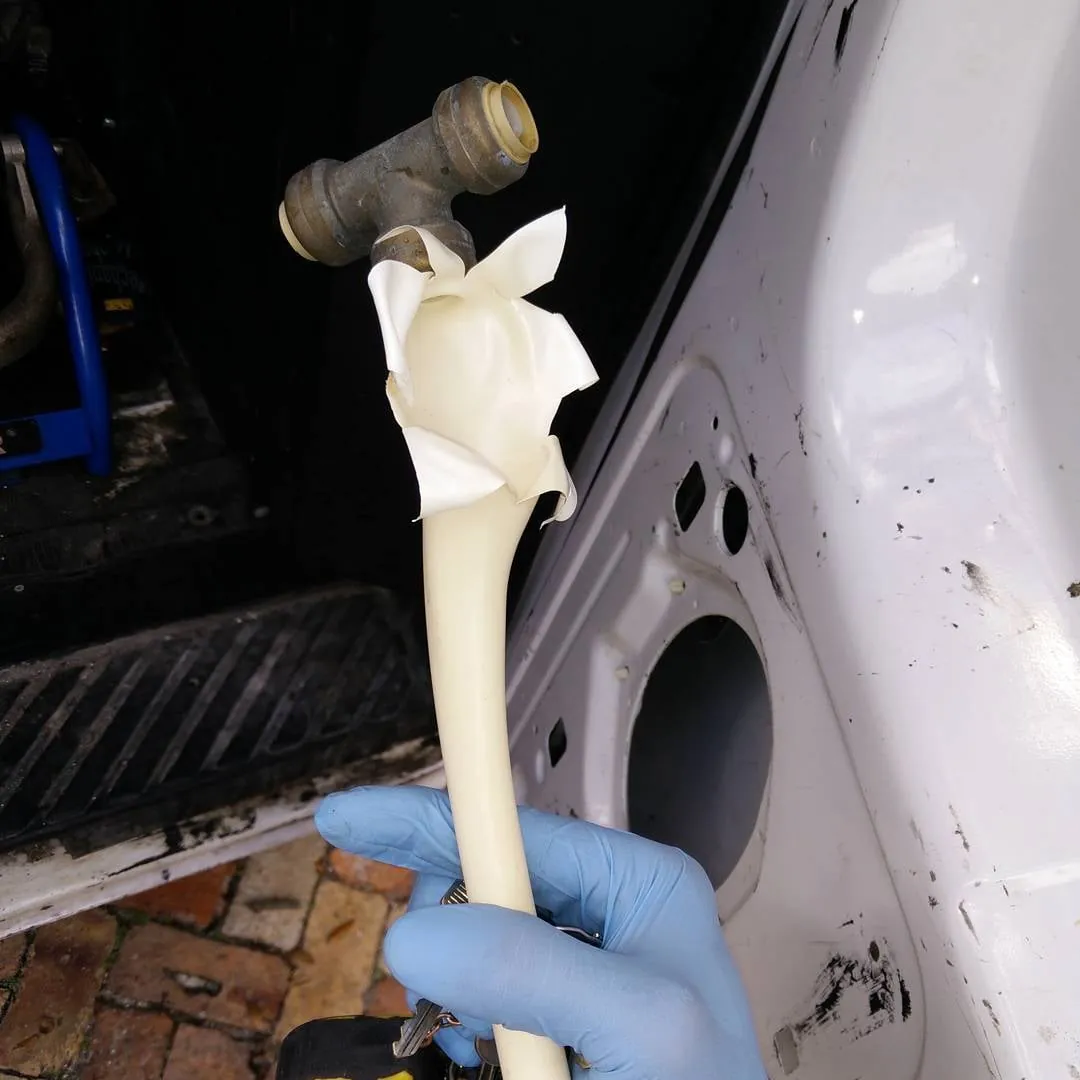Gloved hand holding a failed fitting cut out of a burst water line