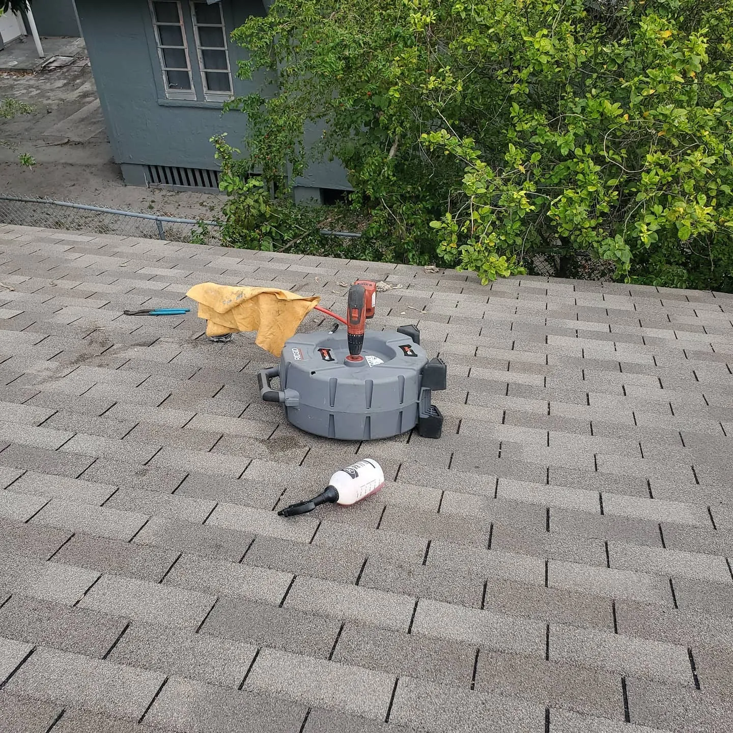 Flexshaft machine with a drill set up on a shingle roof beside a spray bottle