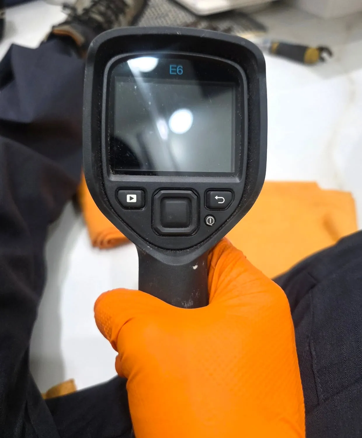 A gloved hand holding a FLIR E6 thermal imaging camera