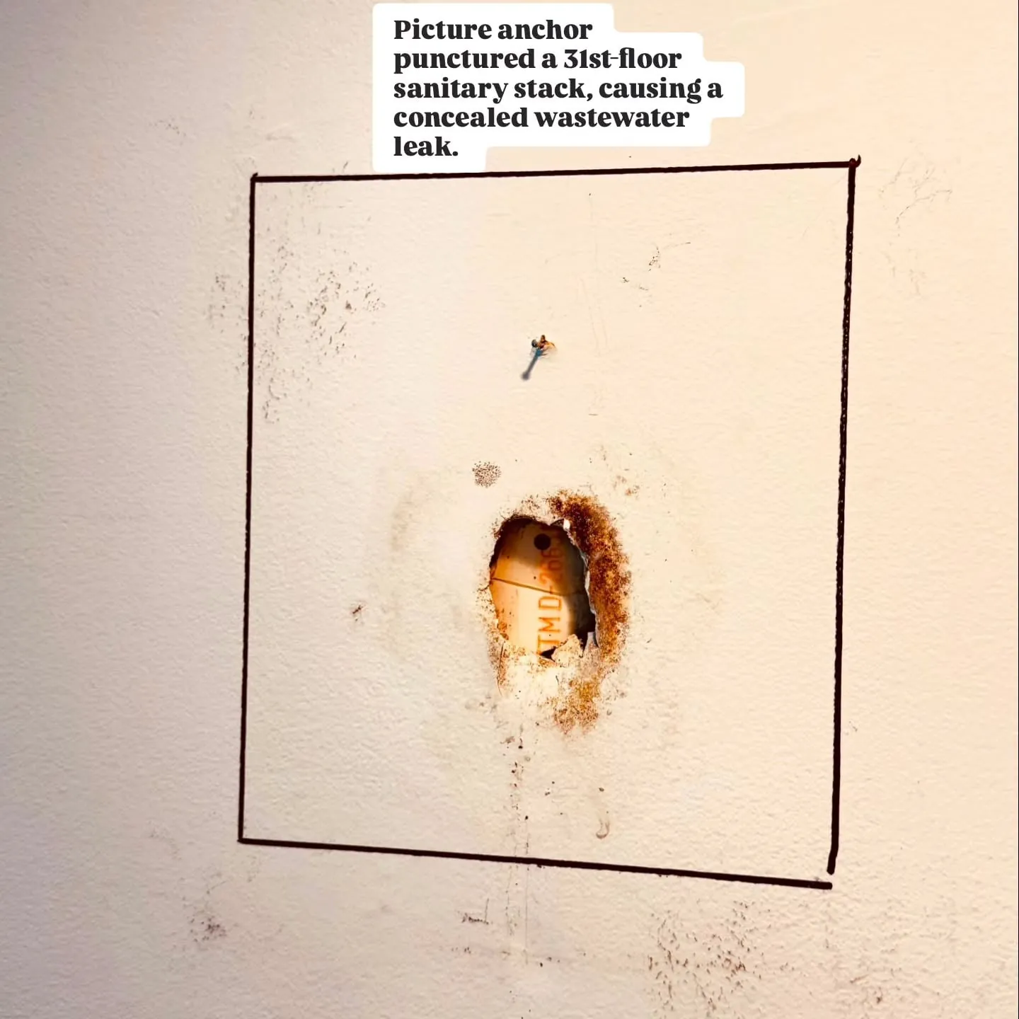 Wall with a small rust-stained hole where a picture anchor punctured a sanitary stack, outlined in marker