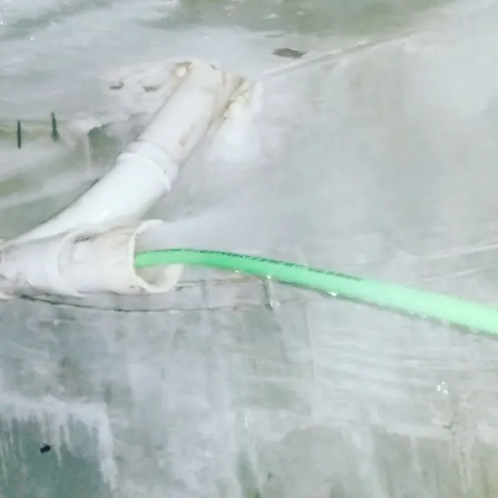 Green jetting hose entering a white PVC line with water spraying back out of the joint