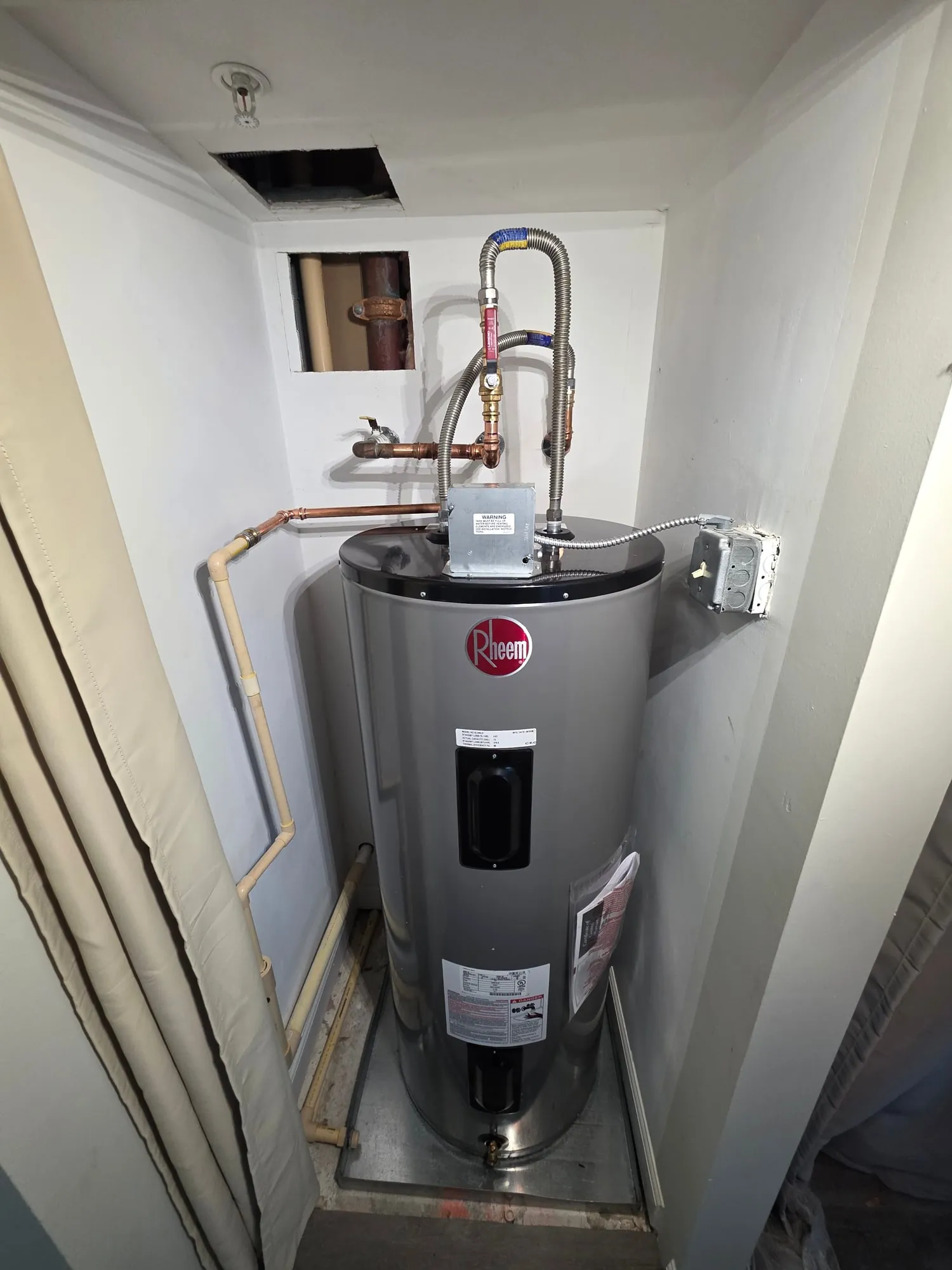 New Rheem electric water heater in a closet with fresh copper piping and braided flex connectors
