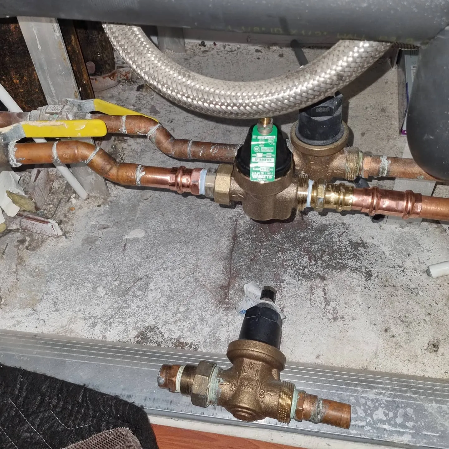 New Watts pressure reducing valve with a green tag on press-fit copper, the old valve set below it