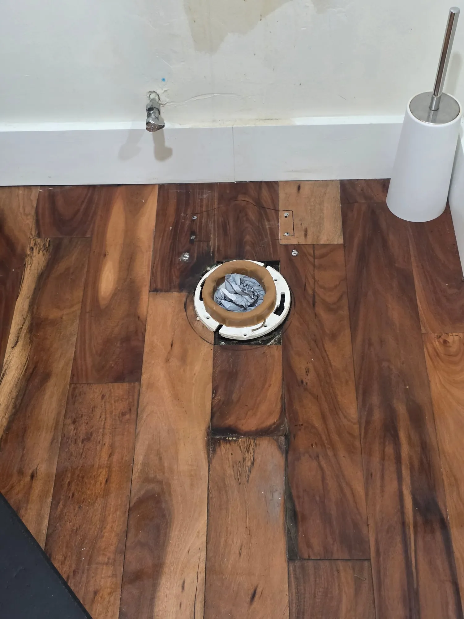 New wax ring seated on a white toilet flange in a hardwood floor