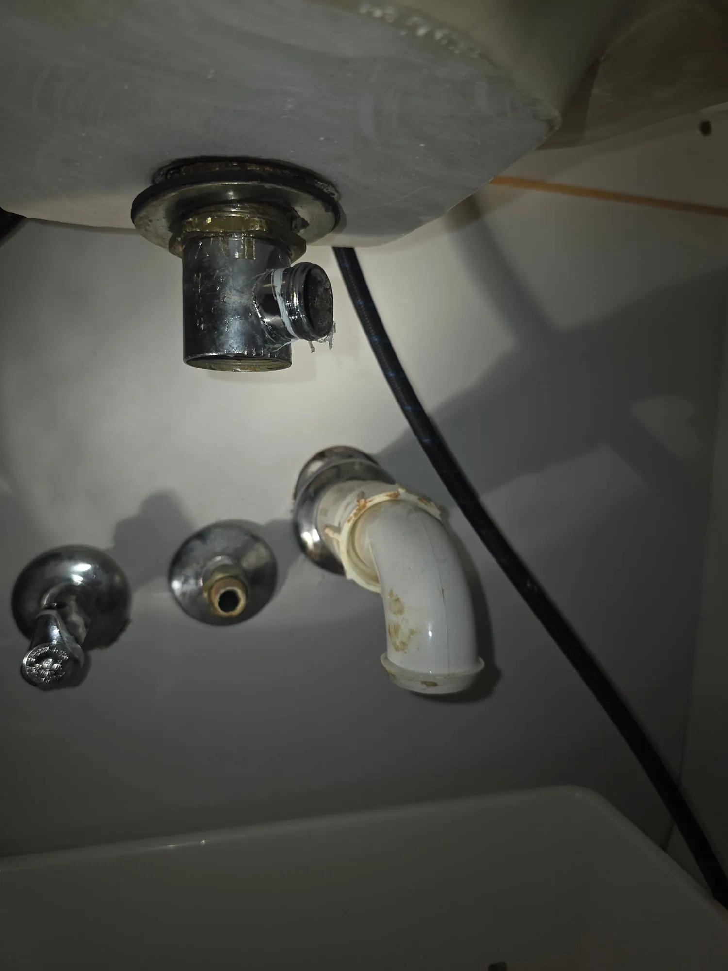 Underside of a sink showing the drain, a chrome angle stop and a trap arm