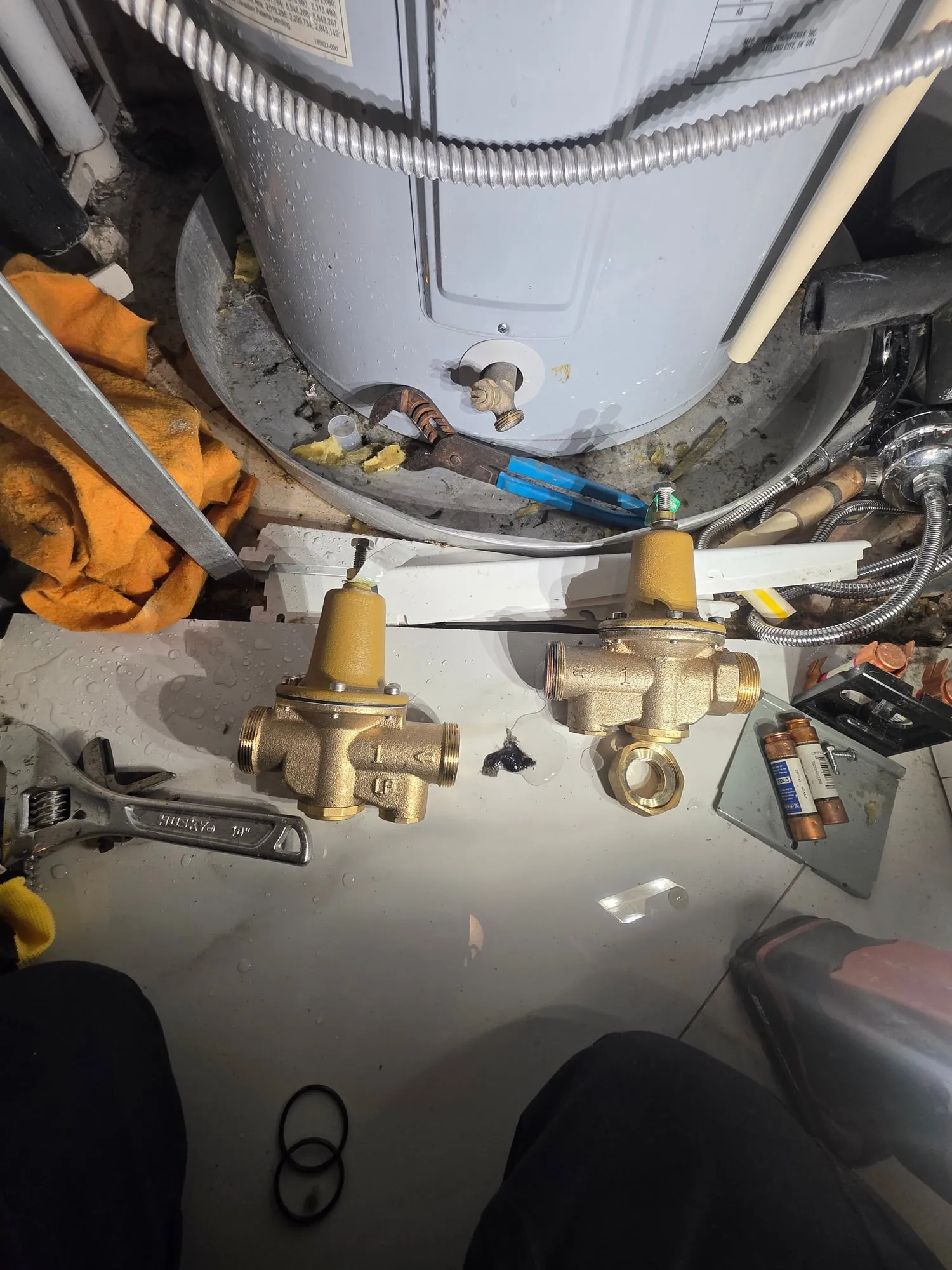 Two bronze pressure reducing valves and an adjustable wrench on the pan beside a water heater