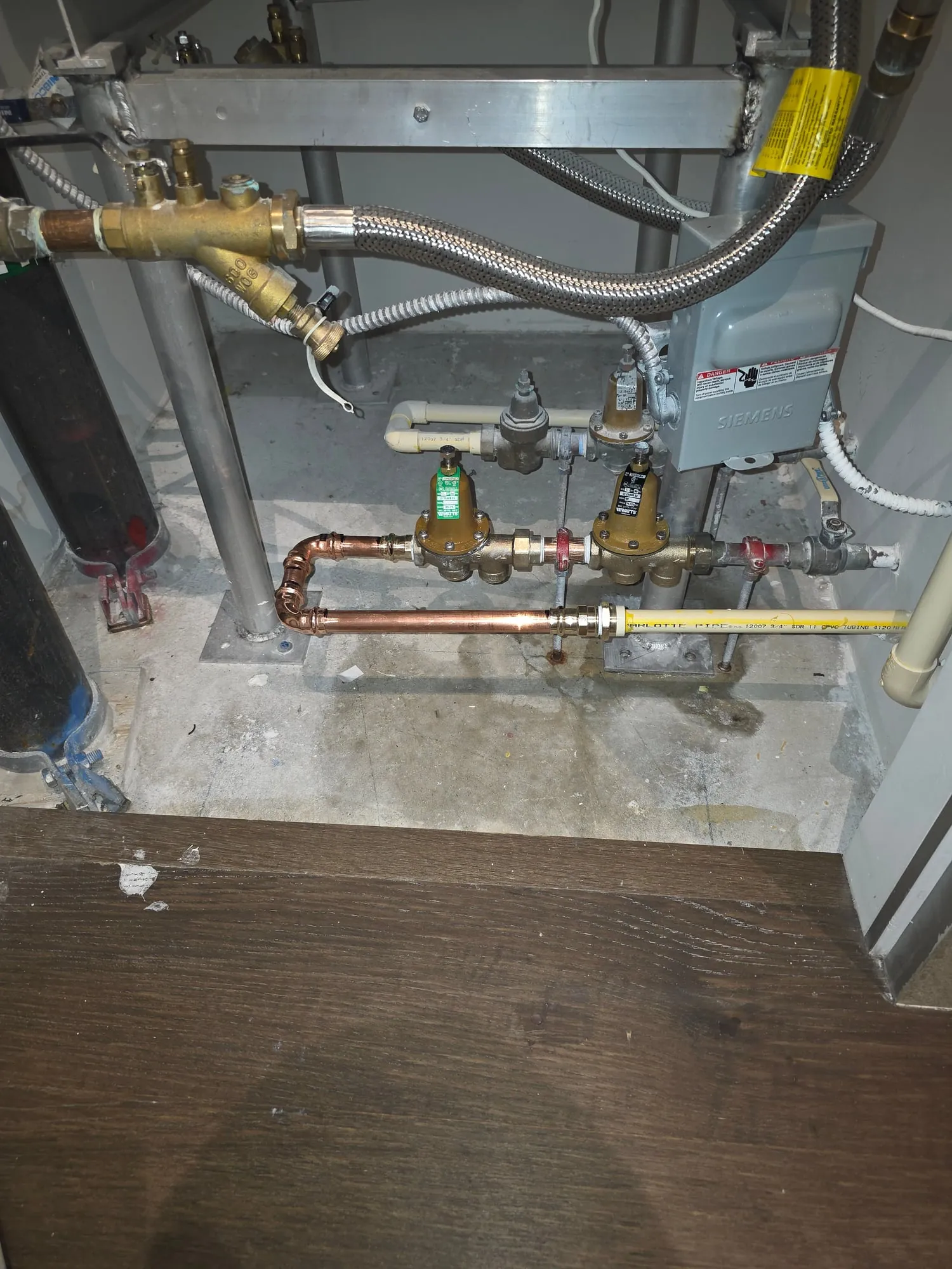 Two pressure reducing valves with a strainer and braided hoses on piping in a mechanical room