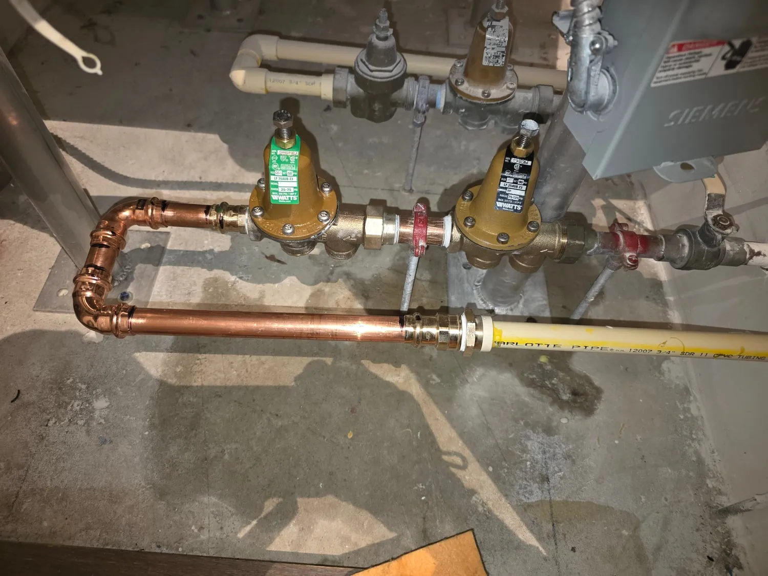Two pressure reducing valves on new press-fit copper piping beside a yellow pipe run
