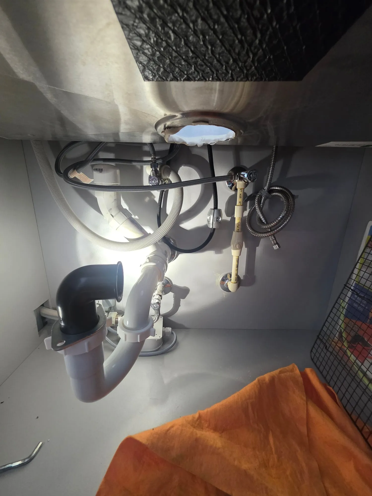 Under a kitchen sink: braided supply lines on chrome angle stops, a white PVC trap and a dishwasher drain hose