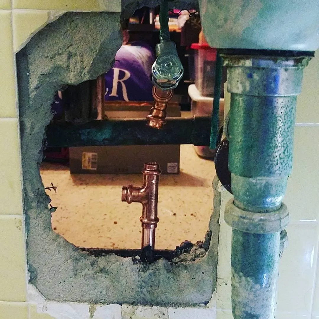 Wall opening with a press-fit copper tee and a stop valve beside an old drain pipe