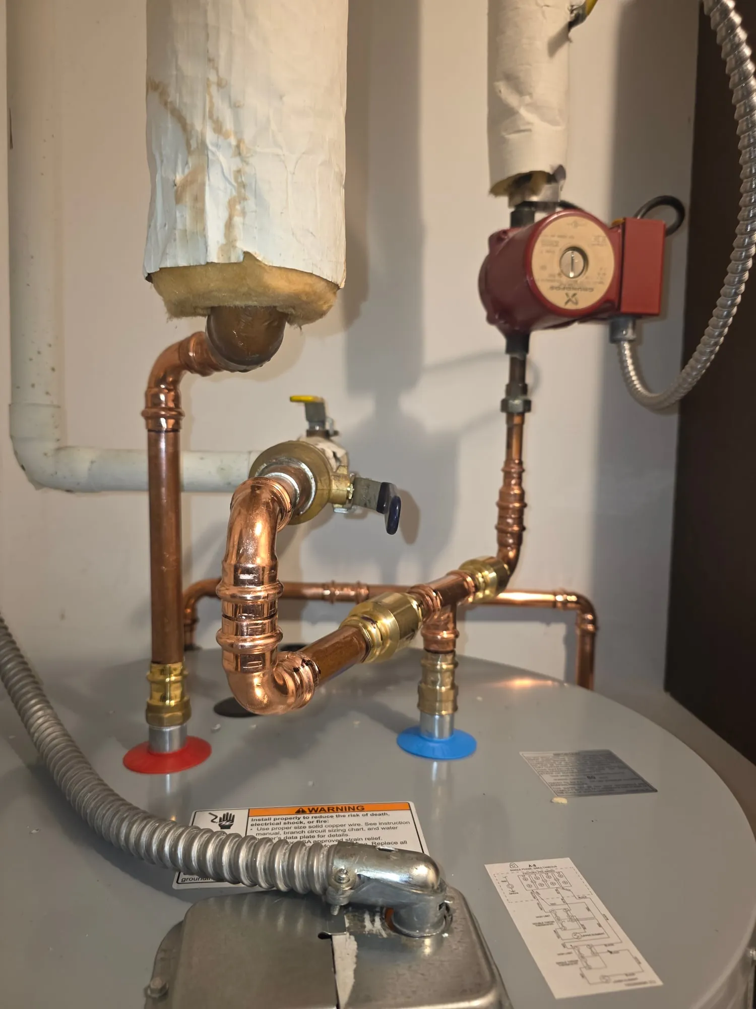 Press-fit copper piping and a red recirculation pump above an electric water heater