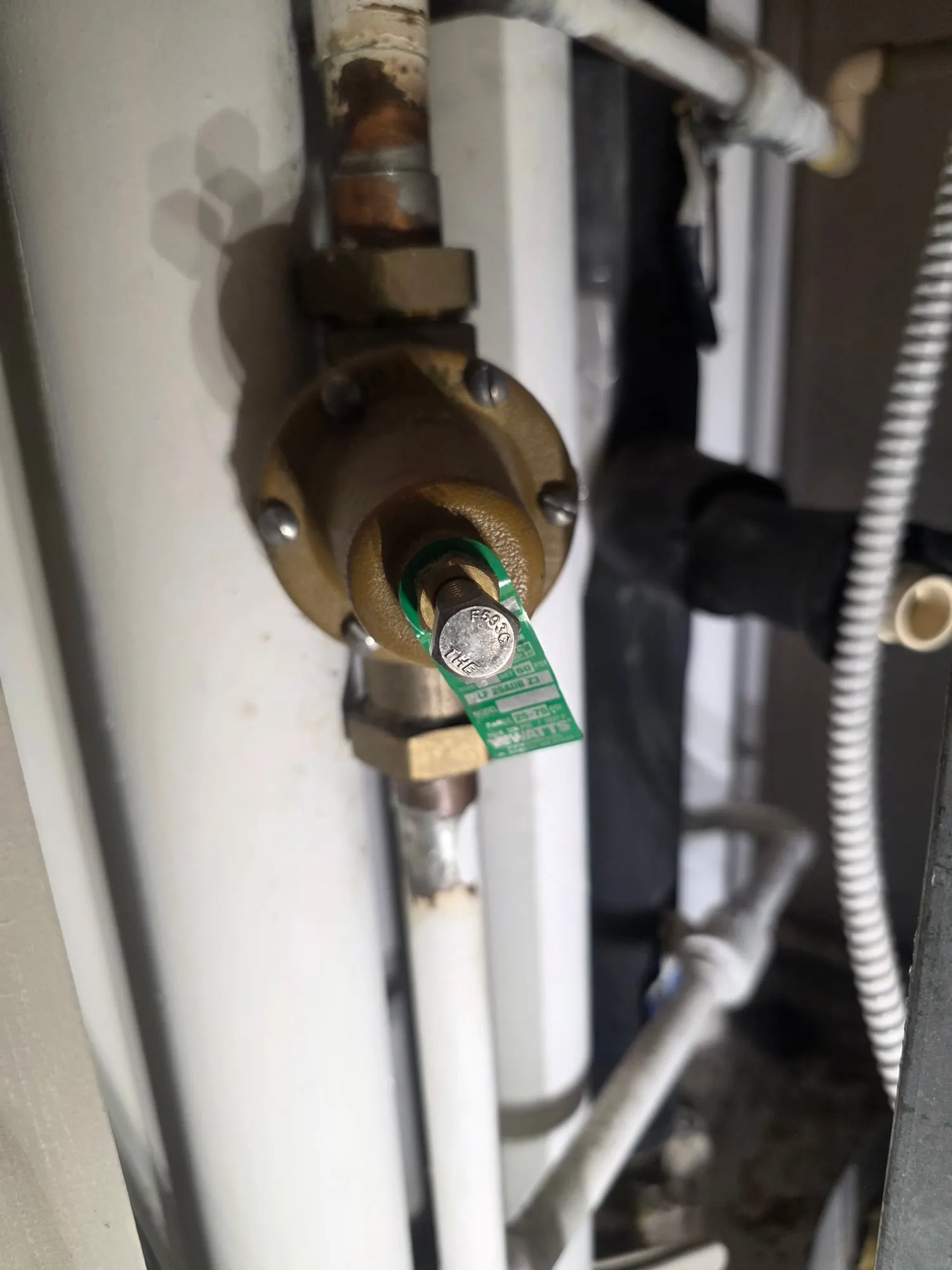 Close-up of a bronze pressure reducing valve with a green Watts tag on a vertical water line